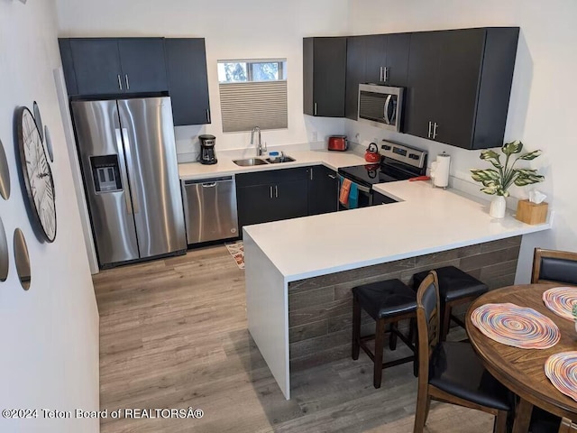 kitchen with a breakfast bar, sink, kitchen peninsula, light hardwood / wood-style flooring, and stainless steel appliances