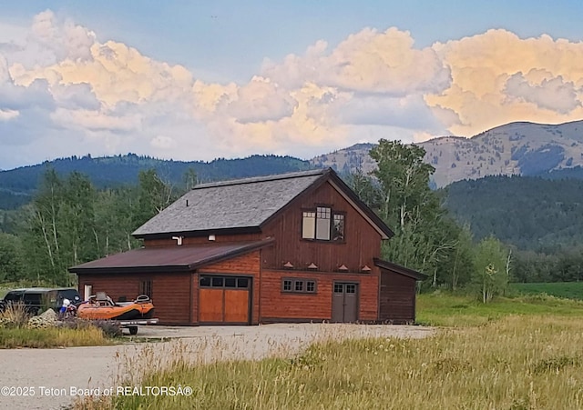 exterior space featuring a mountain view, a detached garage, a barn, and a wooded view