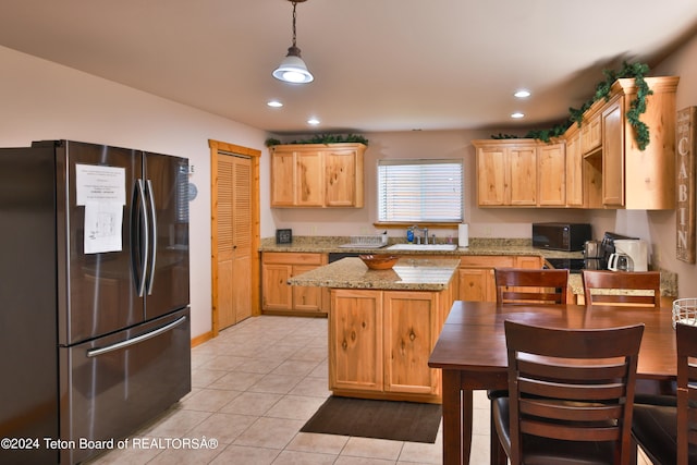 kitchen with light stone counters, light tile patterned flooring, stainless steel fridge, sink, and decorative light fixtures