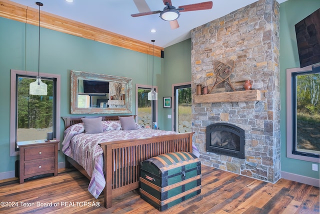 bedroom with ceiling fan, dark hardwood / wood-style floors, multiple windows, and a stone fireplace