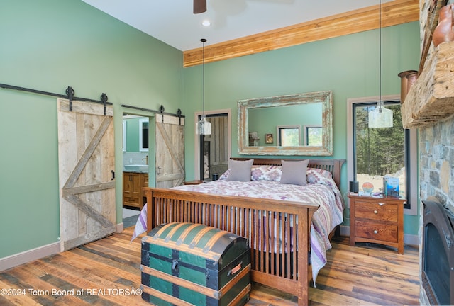 bedroom featuring ceiling fan, hardwood / wood-style flooring, ensuite bath, a barn door, and beam ceiling