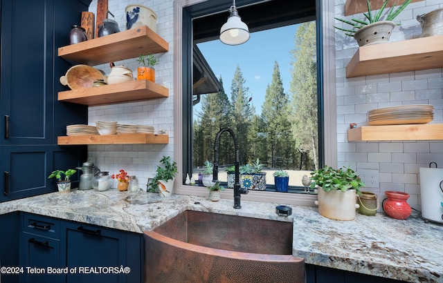 kitchen with light stone counters, blue cabinets, sink, and backsplash