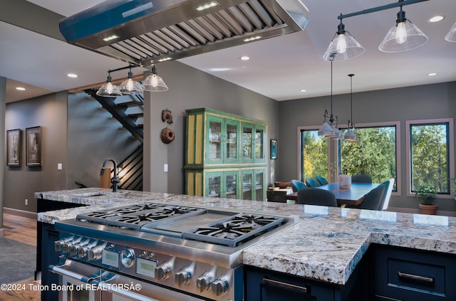 kitchen with light stone countertops, exhaust hood, sink, and blue cabinetry