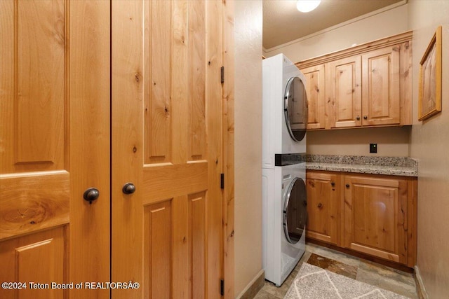 clothes washing area with baseboards, stacked washer and clothes dryer, ornamental molding, and cabinet space