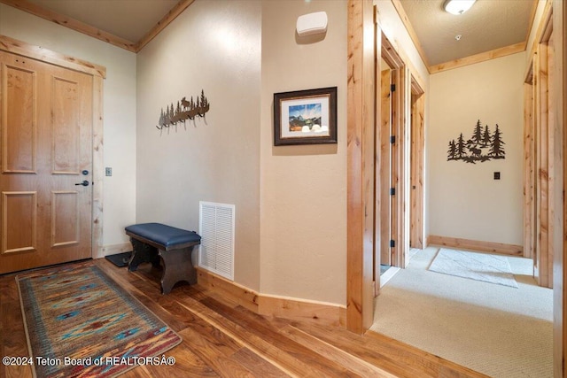 entryway featuring baseboards, crown molding, wood finished floors, and visible vents