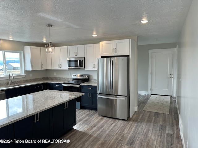 kitchen featuring appliances with stainless steel finishes, pendant lighting, sink, white cabinets, and light hardwood / wood-style floors