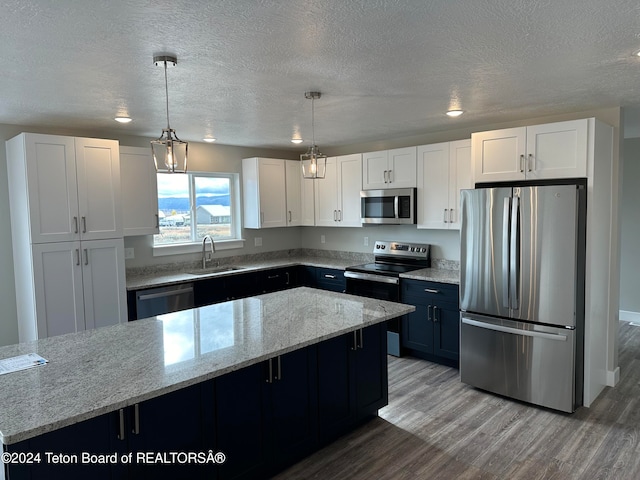 kitchen featuring a kitchen island, pendant lighting, white cabinets, light stone counters, and stainless steel appliances