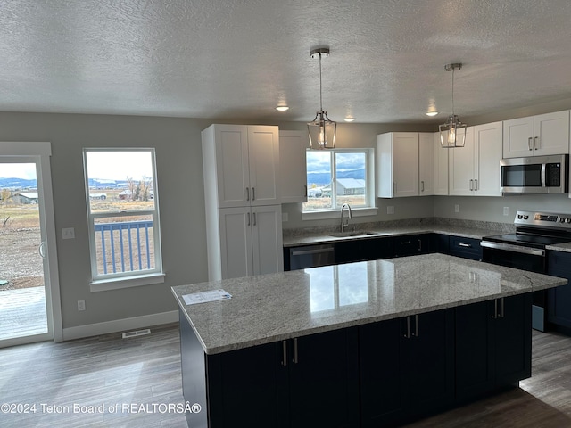 kitchen with sink, appliances with stainless steel finishes, hanging light fixtures, white cabinets, and a kitchen island