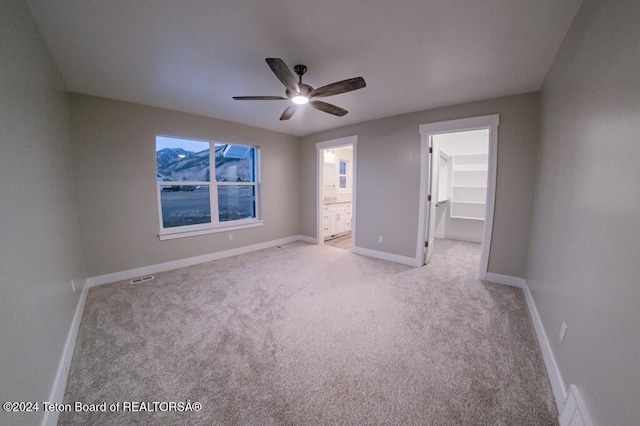 unfurnished bedroom featuring connected bathroom, a spacious closet, light carpet, a closet, and ceiling fan