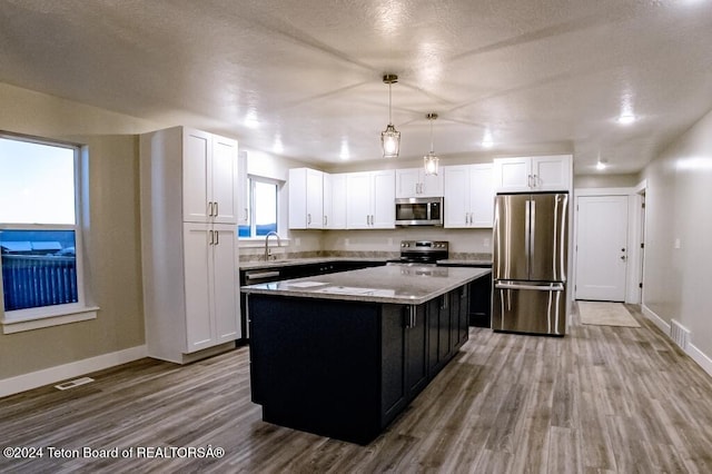 kitchen with white cabinetry, appliances with stainless steel finishes, a kitchen island, pendant lighting, and light hardwood / wood-style floors