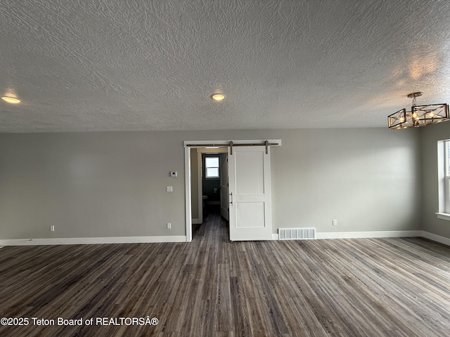 unfurnished room featuring dark wood-type flooring, a barn door, an inviting chandelier, and a textured ceiling