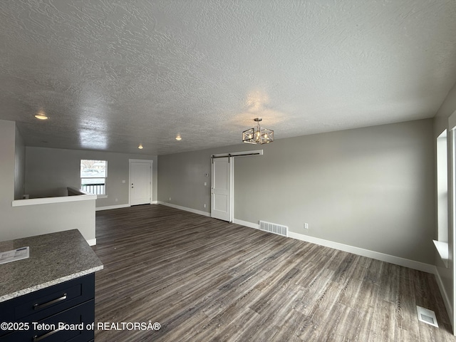 unfurnished living room featuring dark hardwood / wood-style floors, a barn door, and a textured ceiling