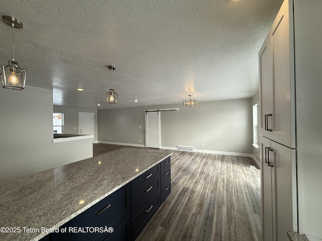 kitchen featuring pendant lighting, white cabinetry, dark hardwood / wood-style flooring, light stone counters, and a barn door