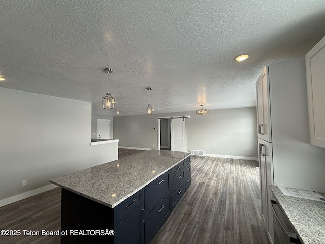 kitchen with a kitchen island, decorative light fixtures, light stone counters, a barn door, and dark wood-type flooring