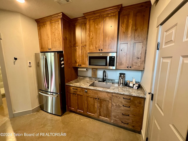 kitchen featuring appliances with stainless steel finishes, light stone countertops, sink, and a textured ceiling