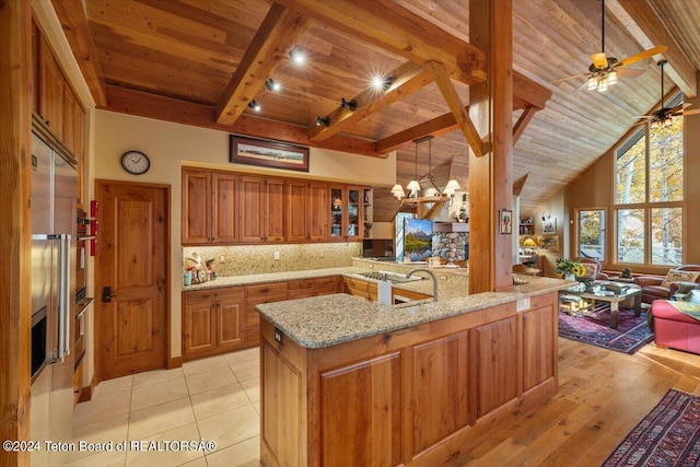 kitchen with light stone counters, beam ceiling, decorative light fixtures, high vaulted ceiling, and light hardwood / wood-style floors