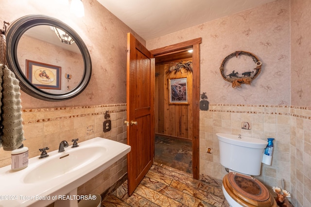 65 Bald Mountain Rd, Dubois, WY 82513 - bathroom with stone finish flooring, toilet, wallpapered walls, a wainscoted wall, and tile walls