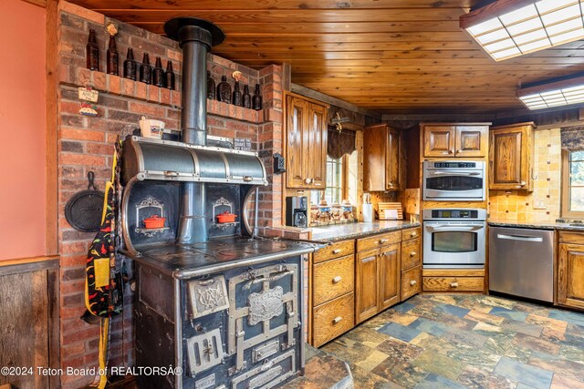 kitchen with appliances with stainless steel finishes, dark stone counters, a wood stove, and wood ceiling