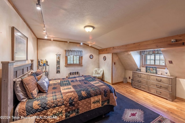 bedroom featuring light hardwood / wood-style floors, radiator, track lighting, vaulted ceiling, and a textured ceiling