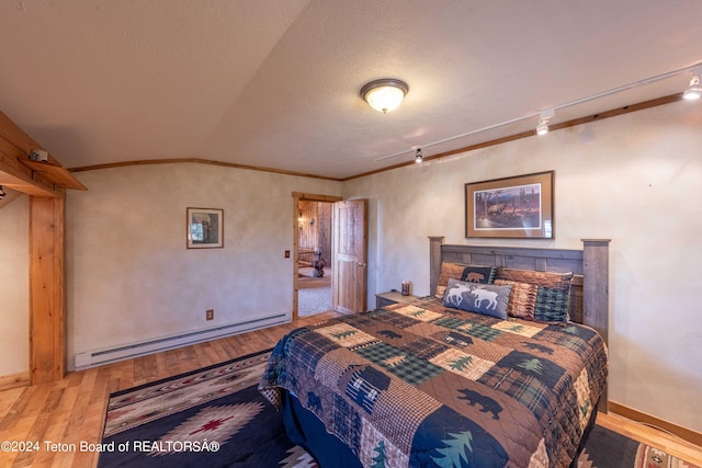 bedroom with hardwood / wood-style floors, rail lighting, a baseboard heating unit, vaulted ceiling, and a textured ceiling