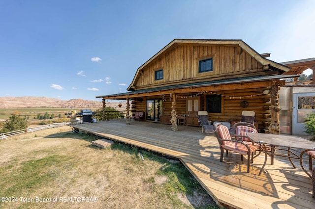 rear view of property with a deck with mountain view and a yard