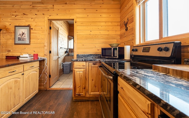 kitchen featuring dark stone countertops, wooden walls, dark hardwood / wood-style flooring, and black range with electric cooktop