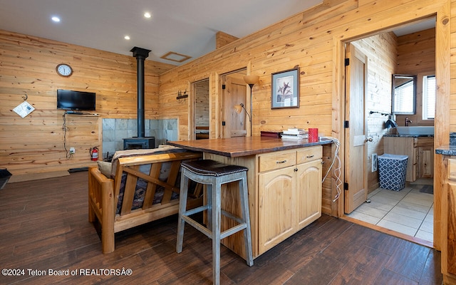 kitchen with light brown cabinets, wooden walls, dark wood-type flooring, and a wood stove