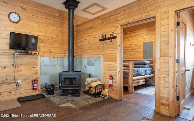 living room featuring electric panel, tile walls, wooden walls, a wood stove, and hardwood / wood-style flooring