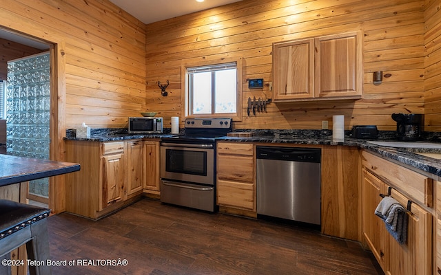 kitchen featuring wood walls, dark stone countertops, dark wood-type flooring, and appliances with stainless steel finishes