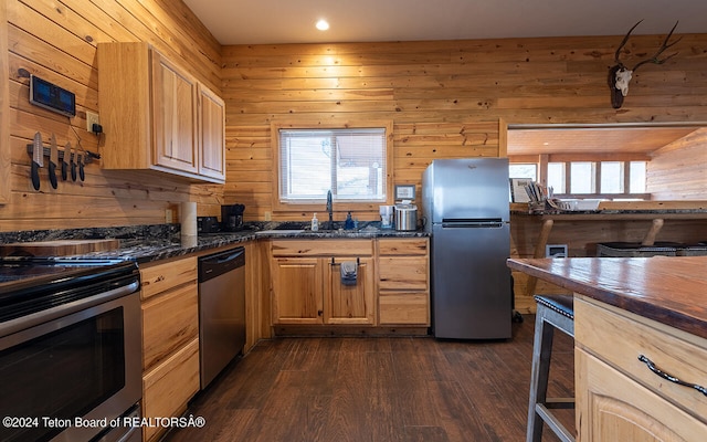 kitchen with wooden walls, stainless steel appliances, light brown cabinets, dark wood-type flooring, and sink