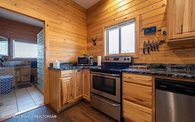 kitchen with dark stone countertops, dark tile patterned floors, appliances with stainless steel finishes, and wooden walls