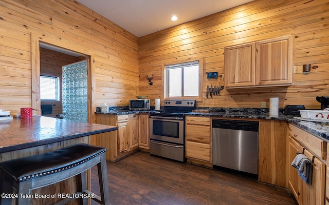 kitchen featuring dark stone counters, wood walls, stainless steel appliances, and dark hardwood / wood-style flooring