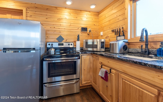 kitchen with dark hardwood / wood-style floors, sink, dark stone counters, appliances with stainless steel finishes, and wood walls