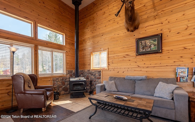 tiled living room with a wood stove, wooden walls, and a towering ceiling