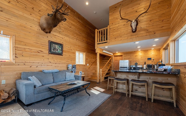 living room with a towering ceiling, sink, dark hardwood / wood-style floors, and wood walls