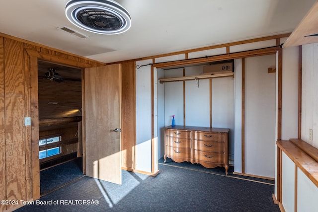 unfurnished bedroom with a closet, wooden walls, and dark colored carpet