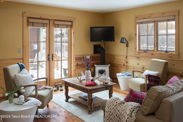 living room with french doors, a wood stove, wood-type flooring, and wooden walls