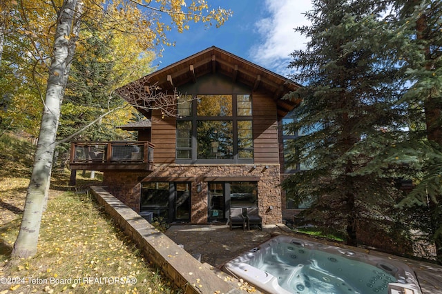 back of property with a balcony, a patio, and an outdoor hot tub