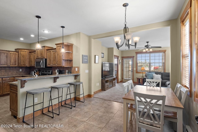 kitchen with backsplash, light stone countertops, decorative light fixtures, a baseboard radiator, and ceiling fan with notable chandelier