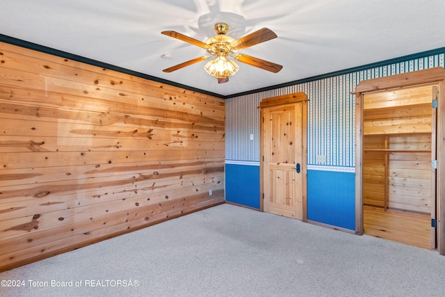 unfurnished bedroom featuring ceiling fan, carpet flooring, crown molding, a closet, and wooden walls