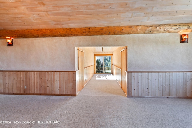 carpeted spare room with beam ceiling, wood walls, and wooden ceiling