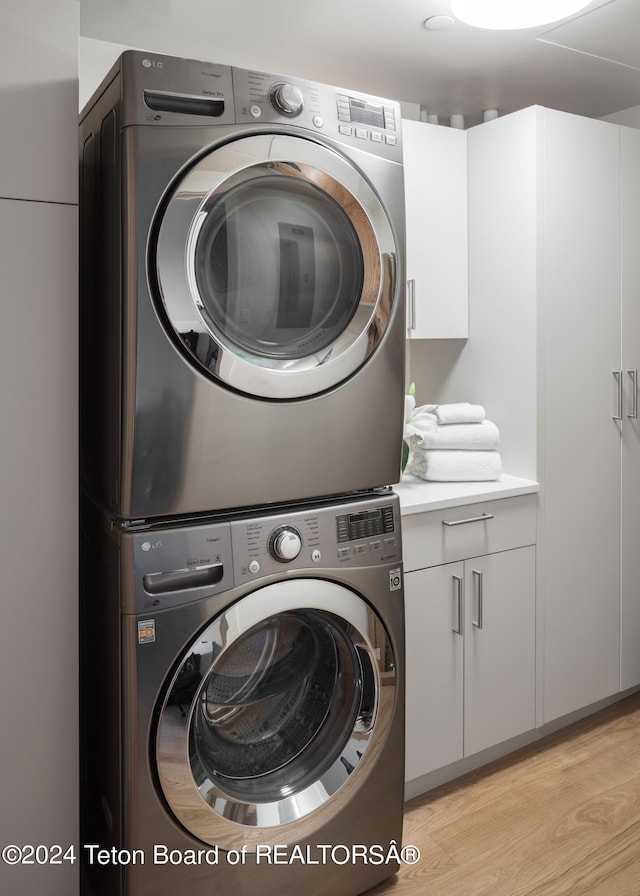 laundry area with stacked washer / drying machine, light hardwood / wood-style floors, and cabinets