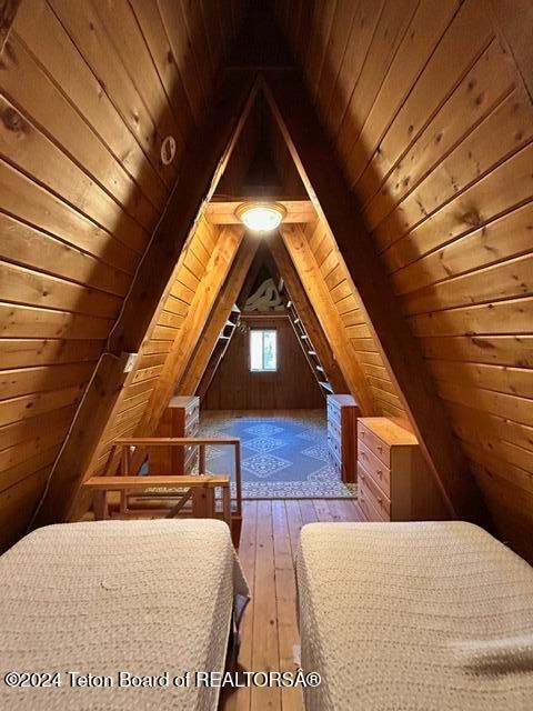 unfurnished bedroom featuring lofted ceiling, hardwood / wood-style flooring, wooden walls, and wooden ceiling