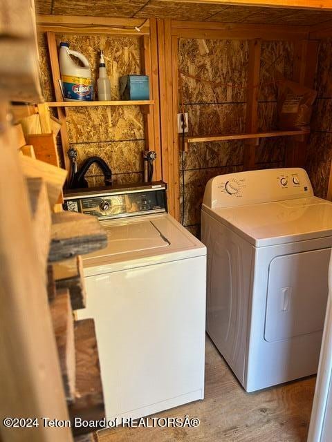 clothes washing area with wood-type flooring, separate washer and dryer, and wood walls