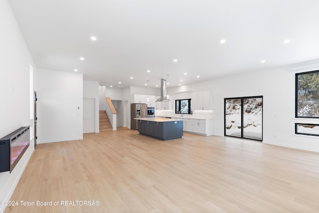 kitchen with island exhaust hood, stainless steel appliances, white cabinetry, light hardwood / wood-style flooring, and a kitchen island