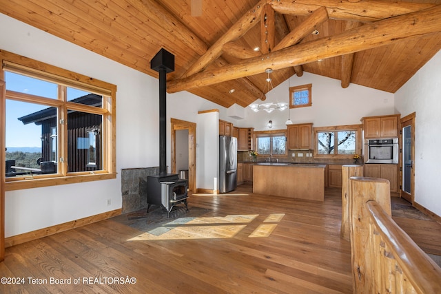 kitchen with a kitchen island, appliances with stainless steel finishes, beamed ceiling, light hardwood / wood-style floors, and a wood stove