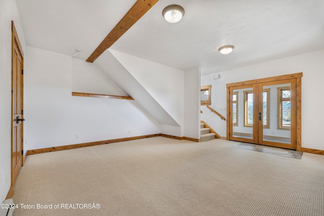 unfurnished living room with vaulted ceiling with beams, french doors, and light carpet