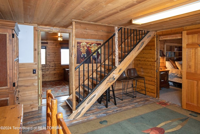 staircase with wooden walls, wooden ceiling, and carpet floors