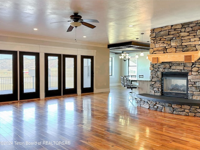 unfurnished living room featuring hardwood / wood-style flooring, ceiling fan with notable chandelier, a stone fireplace, and ornamental molding