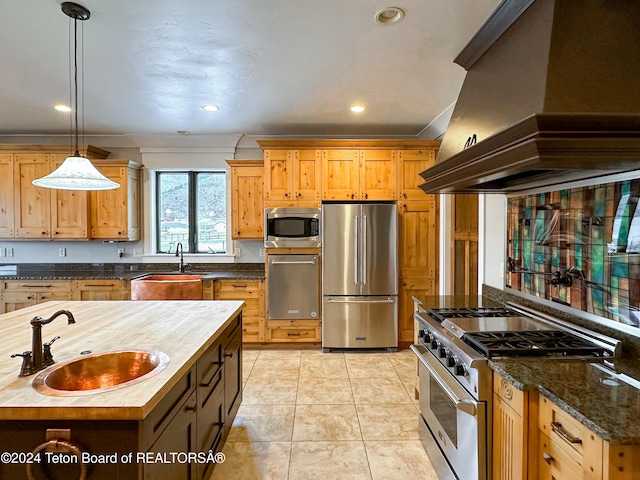 kitchen featuring premium range hood, sink, butcher block countertops, decorative light fixtures, and stainless steel appliances